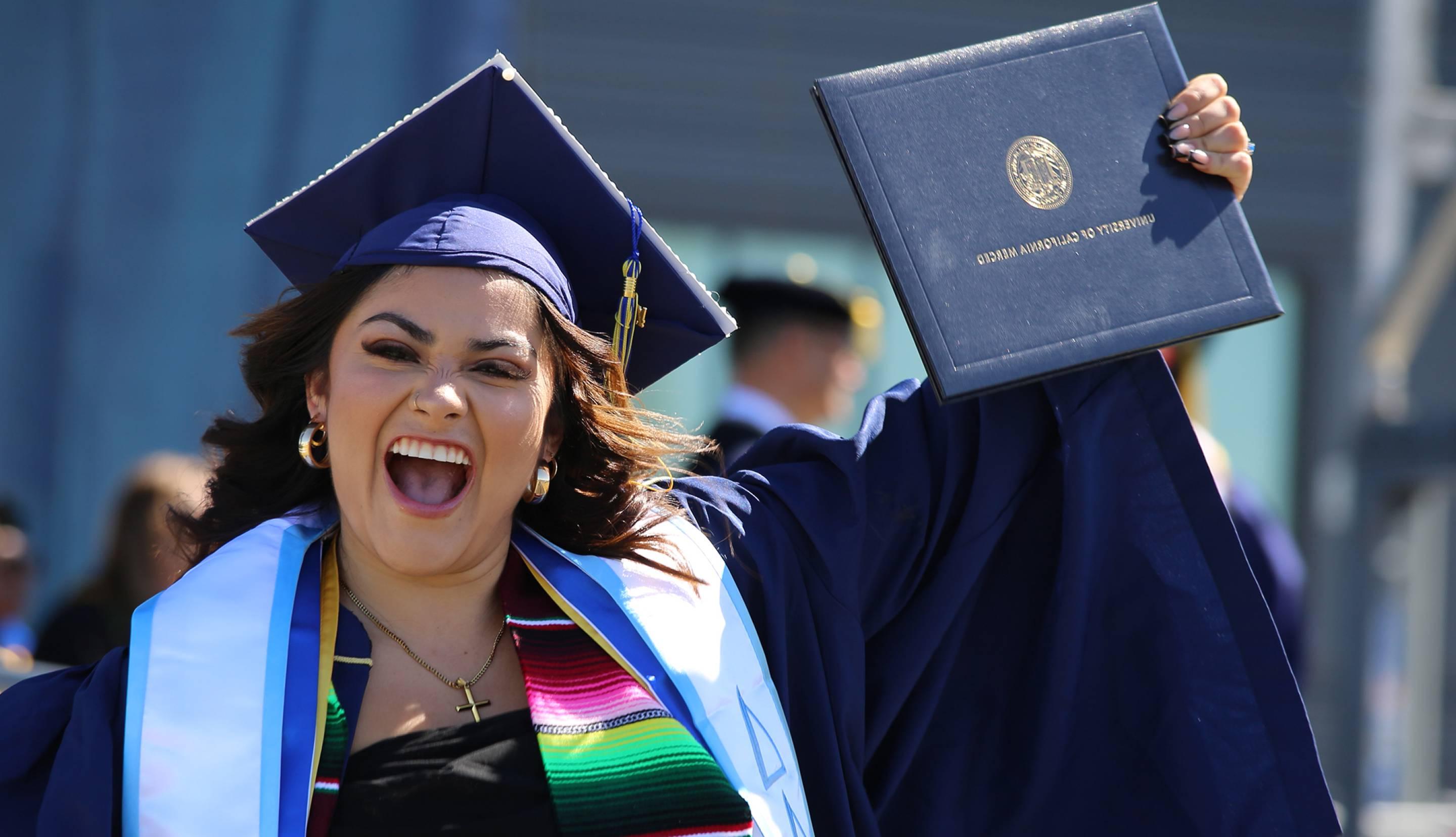 一个快乐的女毕业生拿着她的文凭，带着灿烂的笑容穿过舞台，戴着帽子和长袍